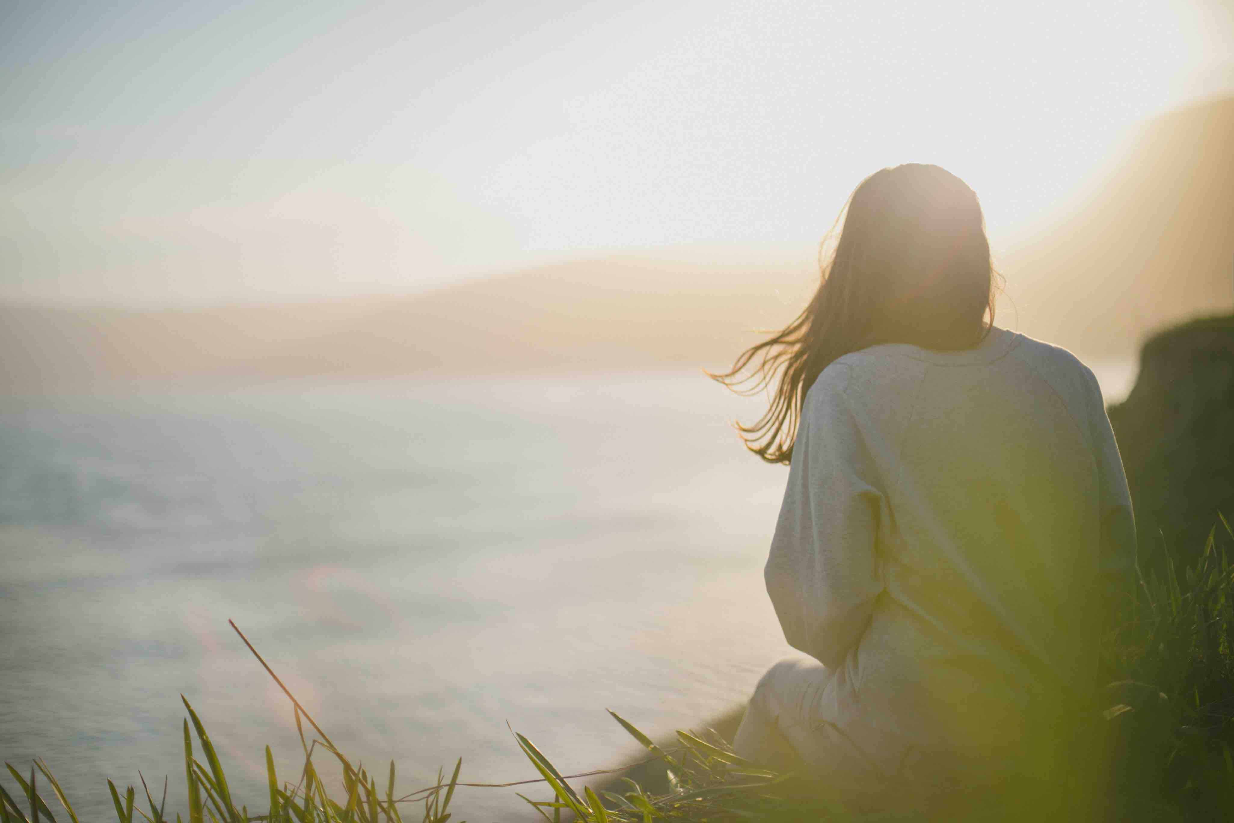 A person sitting on a cliff with their back to the camera, overlooking the ocean.