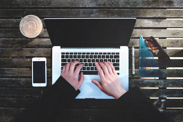 Hands typing on a laptop at an outside table