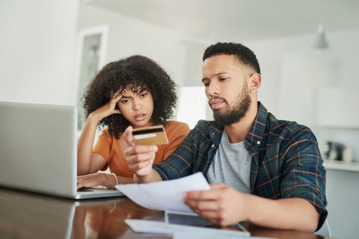 two people looking stressed and holding a credit card up next to a credit card statement