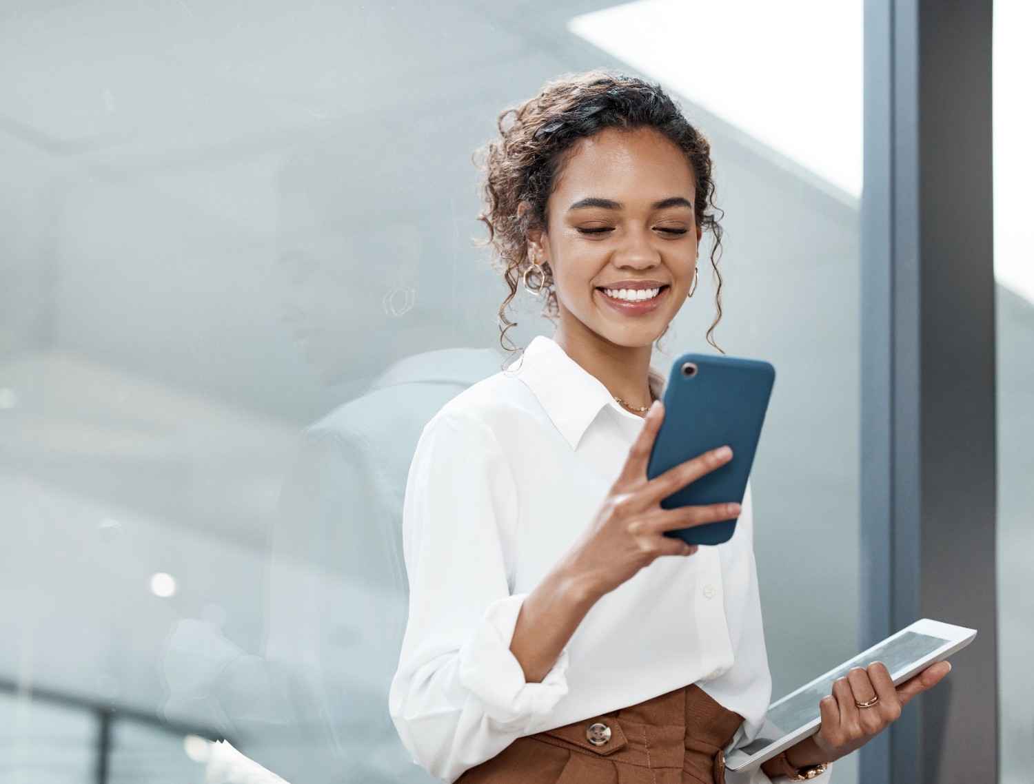 woman looking at her phone and holding a tablet